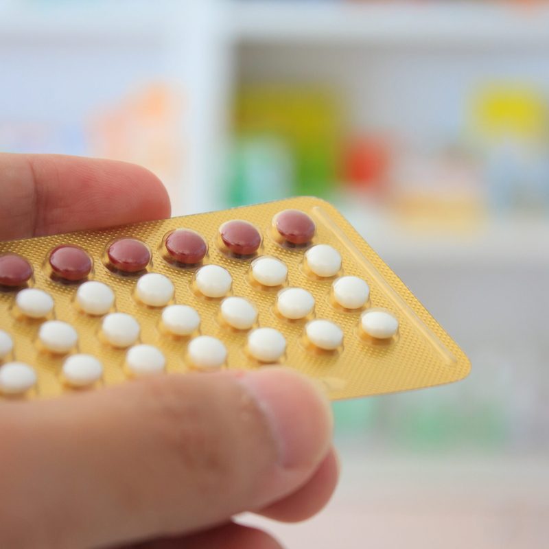 Close up of pharmacist hands holding contraceptive pills with pharmacy store shelves background